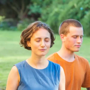 Two people, a young woman and man, eyes closed, peacefully in meditation outdoors
